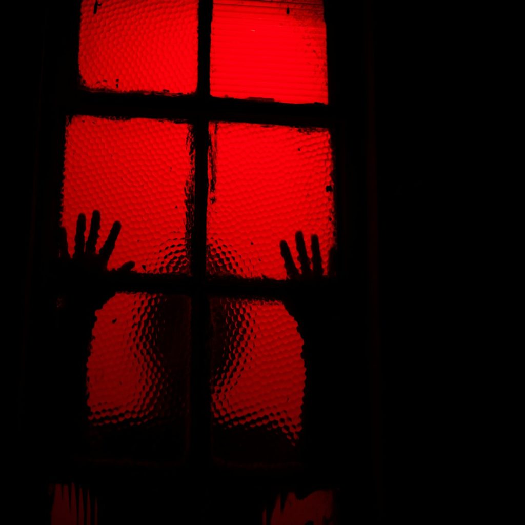 Silhouette of person leaning against window in room with red light
